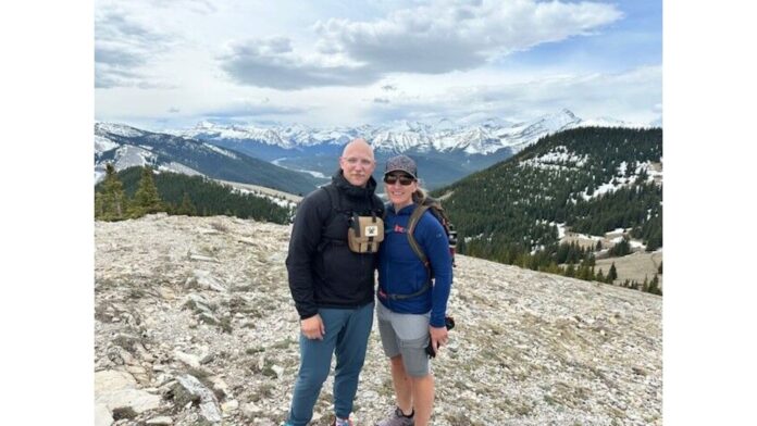 Kathy and her son standing on a hilltop with mountain scenery behind.